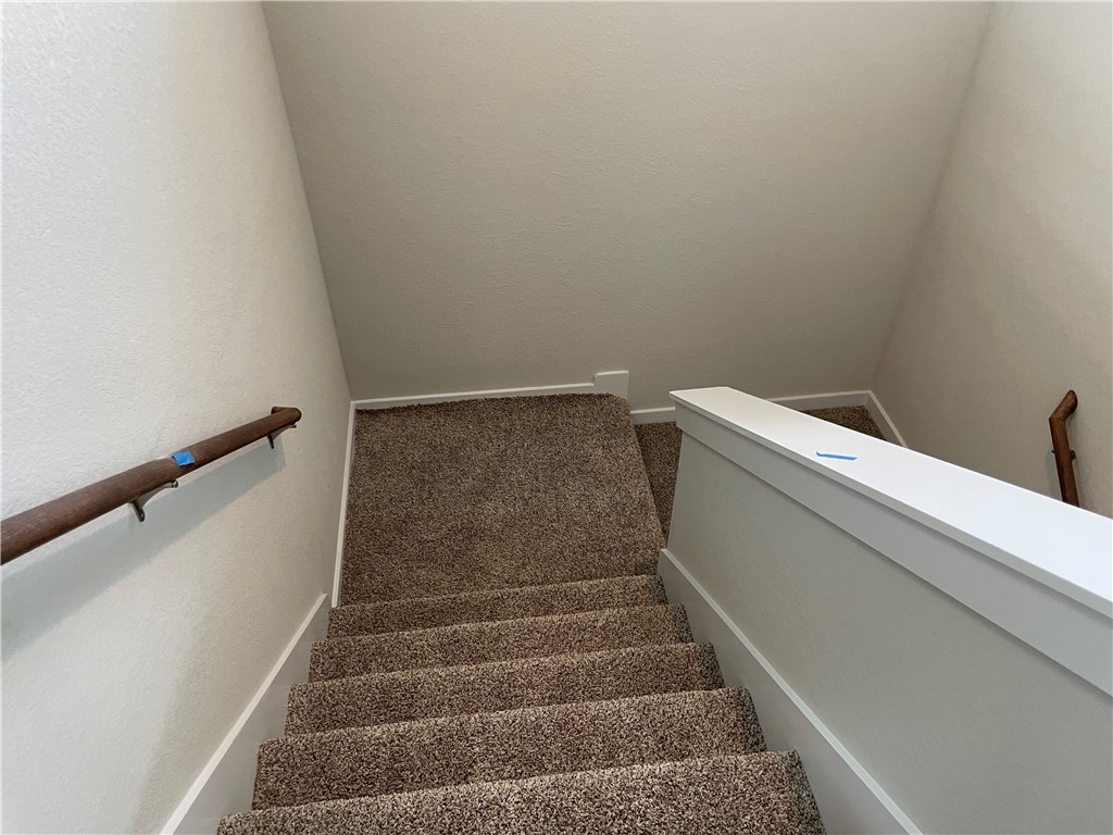 609 Paddock Lane Georgetown, TX 78626 - Photo 32 of 40 A carpeted staircase leads downward between neutral-toned walls equipped with wooden handrails.