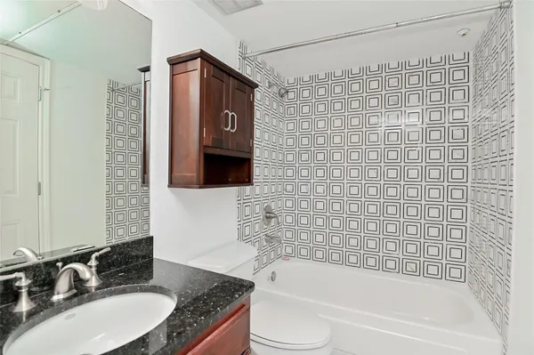 a bathroom with a granite countertop bathtub shower sink vanity and toilet