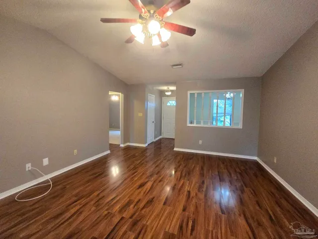 a view of an empty room with wooden floor and a chandelier fan