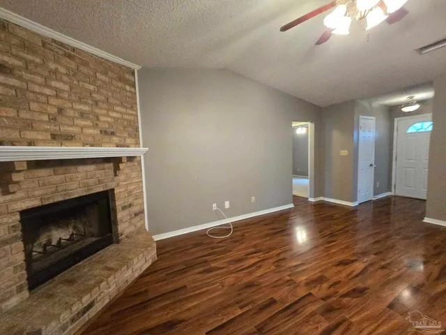 a view of an empty room with wooden floor and a fireplace