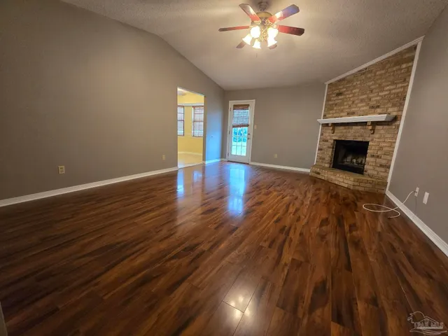 a view of an empty room with wooden floor fireplace and a window