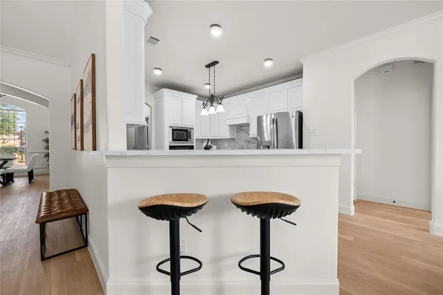 a kitchen with stainless steel appliances granite countertop a sink a stove a refrigerator and chairs with wooden floor