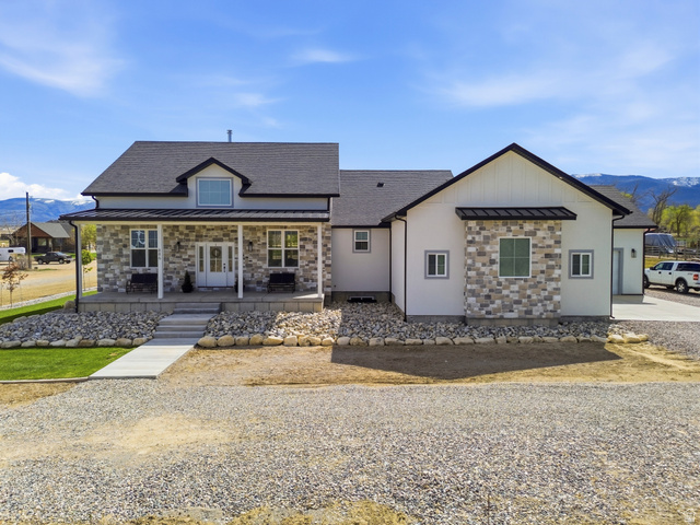 View of front of home featuring a mountain view, a standing seam roof, covered porch, stone siding, and a shingled roof