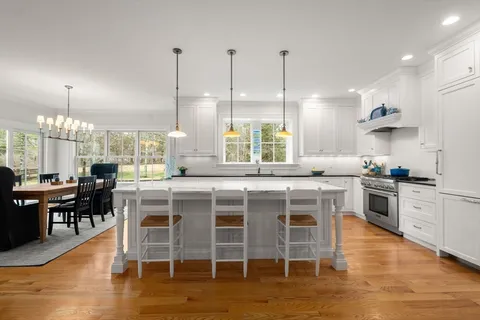 a kitchen with stainless steel appliances granite countertop a stove a sink a oven a dining table and chairs with wooden floor