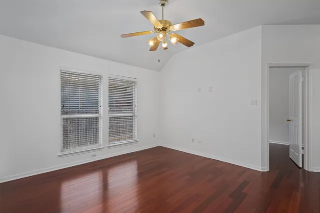 a view of an empty room with wooden floor and a ceiling fan