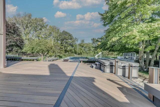 a view of swimming pool that has wooden bench and a lawn chairs with large trees