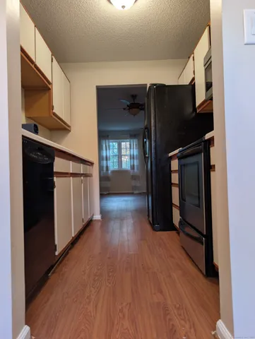 a view of a refrigerator in kitchen and an empty room with wooden floor