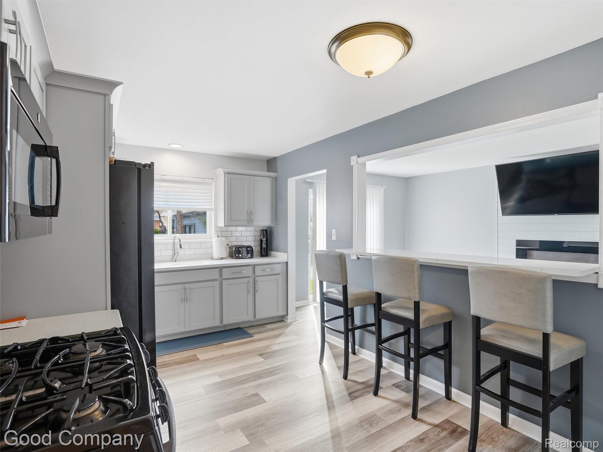 30632 Hayes Road Roseville, MI 48066 - Photo 11 of 32 Kitchen featuring light wood-finish flooring, light gray cabinetry, white subway tile backsplash, and a breakfast bar with solid surface countertop