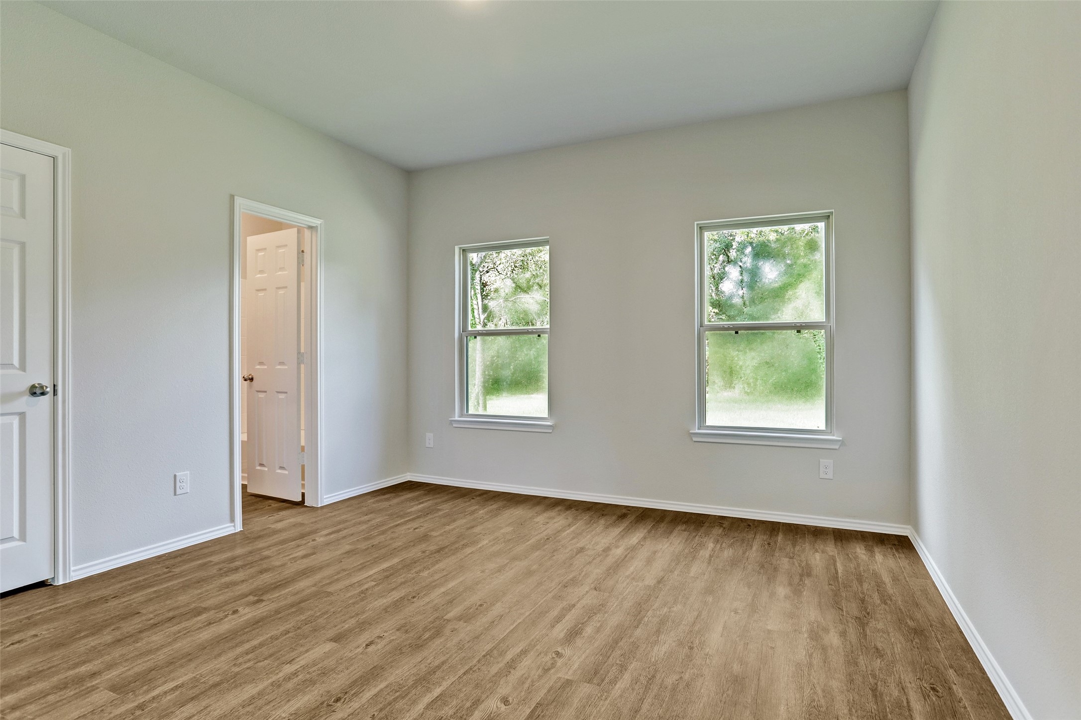 409 South 12th Street, Unit B Conroe, TX 77301 - Photo 9 of 14 Bright room with two large windows offering a view of greenery. Features light-colored walls, wood flooring, and an adjacent doorway leading to another space. Ideal for a bedroom or home office.