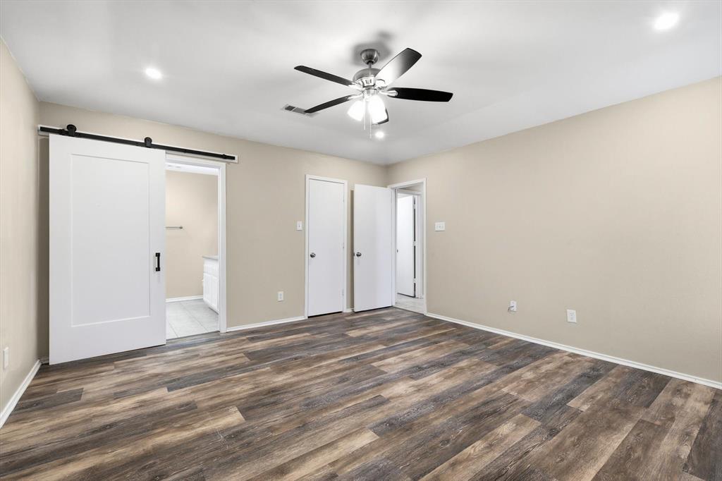 7733 Liz Lane Watauga, TX 76148 - Photo 16 of 27 Unfurnished bedroom featuring a barn door, wood finished floors, connected bathroom, ceiling fan, and recessed lighting