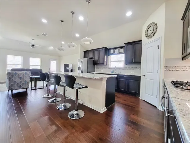 a kitchen with stainless steel appliances granite countertop a stove top oven a sink dishwasher a dining table and chairs with wooden floor