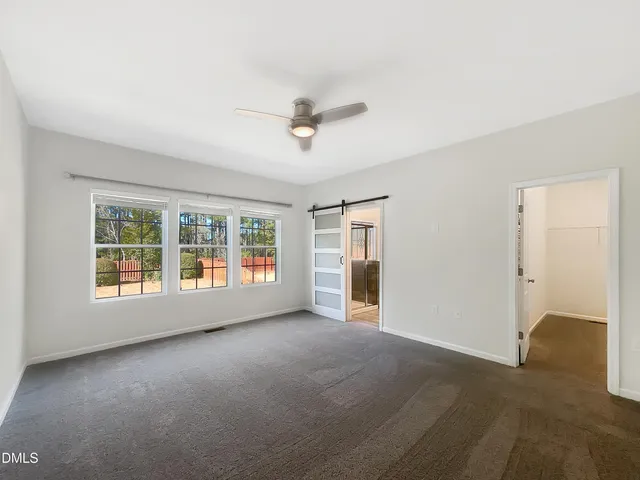 an empty room with chandelier fan and windows