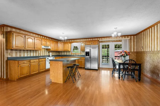 a open kitchen with stainless steel appliances granite countertop a stove top oven a dining table and chairs with wooden floor