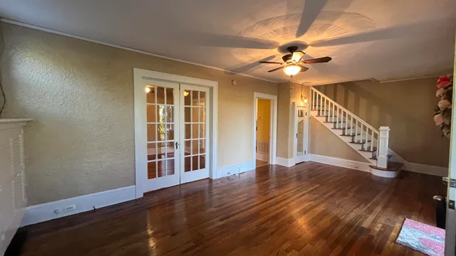 a view of an empty room with wooden floor and a ceiling fan