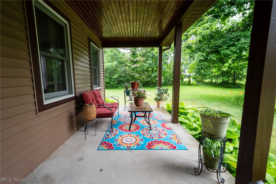 14027 Mayfield Road Huntsburg, OH 44046 - Photo 39 of 50 Covered front porch featuring a concrete pad, brown siding, white window trim, and a wood-finish ceiling