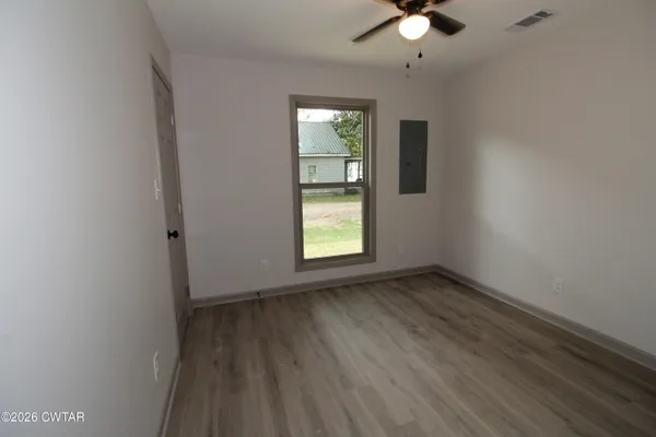 an empty room with wooden floor chandelier fan and windows