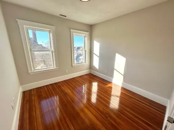 a view of an empty room with wooden floor and window