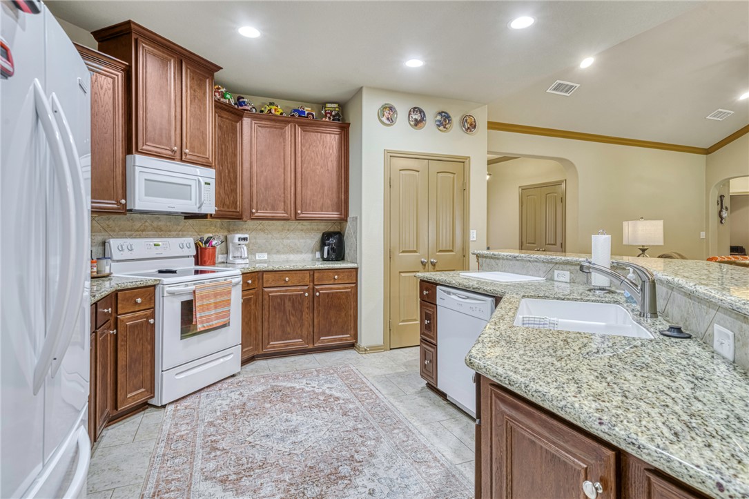 9945 Oxford Cemetery Road Madisonville, TX 77864 - Photo 13 of 42 Kitchen with white appliances, decorative backsplash, arched walkways, light stone countertops, and recessed lighting