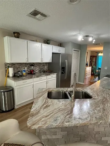 a kitchen with granite countertop a refrigerator oven a sink a stove and white cabinets