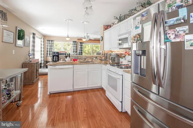 a kitchen with stainless steel appliances a refrigerator a sink dishwasher a stove top oven a dining table and chairs with wooden floor