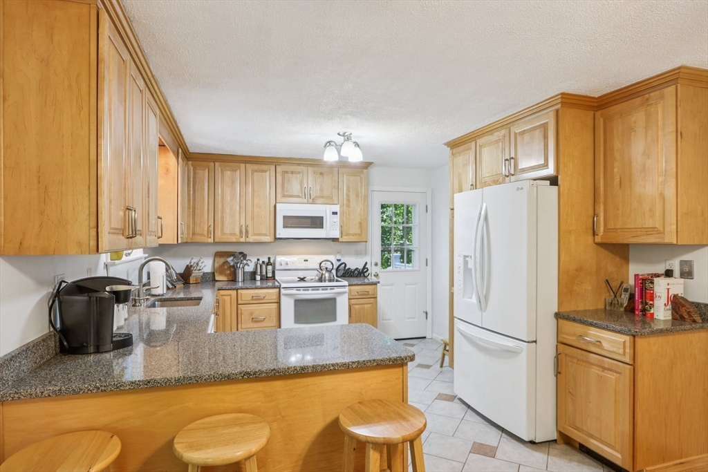 196 Hudson Road Stow, MA 01775 - Photo 9 of 31 a kitchen with granite countertop a refrigerator a stove a sink dishwasher and white cabinets with wooden floor