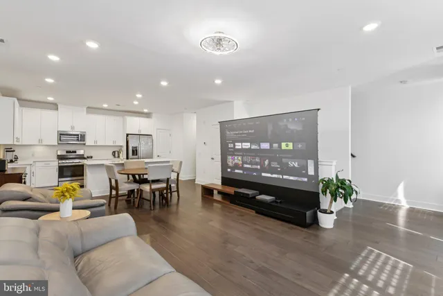 a living room with lots of furniture kitchen view and a large window