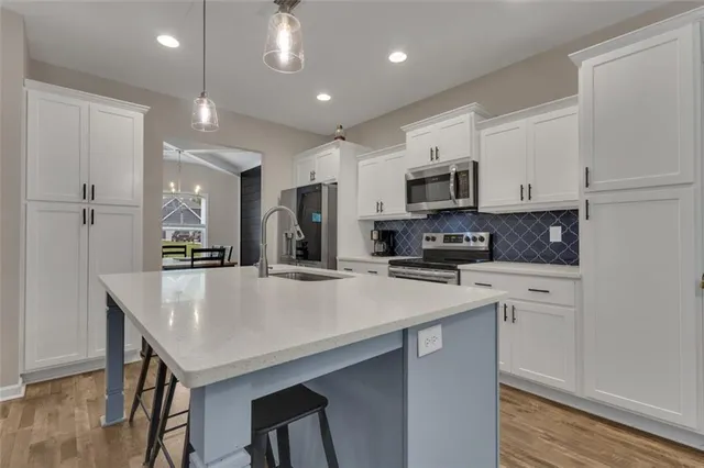 a kitchen with stainless steel appliances granite countertop a refrigerator a stove a microwave oven a sink dishwasher and white cabinets with wooden floor