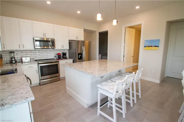 a kitchen with stainless steel appliances kitchen island granite countertop a stove a sink a microwave a refrigerator and chairs