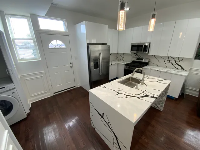a living room with stainless steel appliances furniture wooden floor and a kitchen view