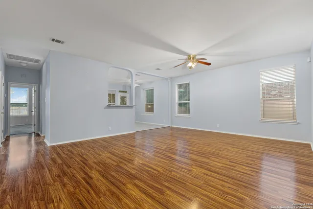 an empty room with wooden floor ceiling fan and windows