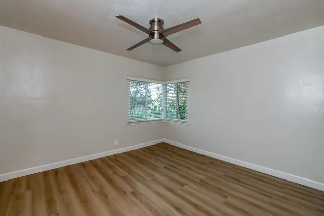 an empty room with wooden floor fan and windows