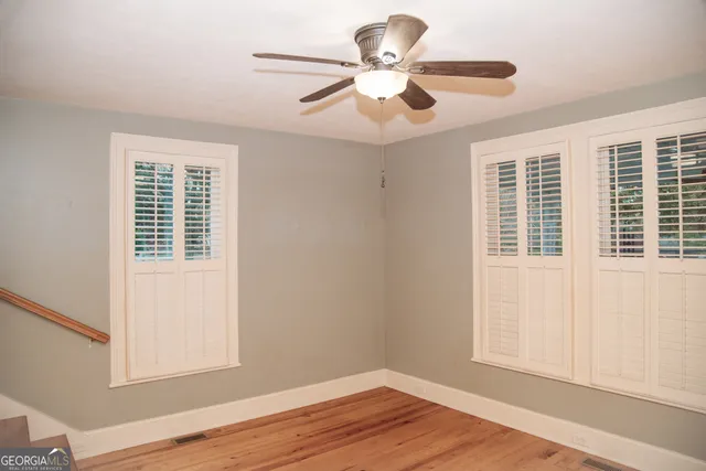 a view of an empty room with wooden floor and a ceiling fan
