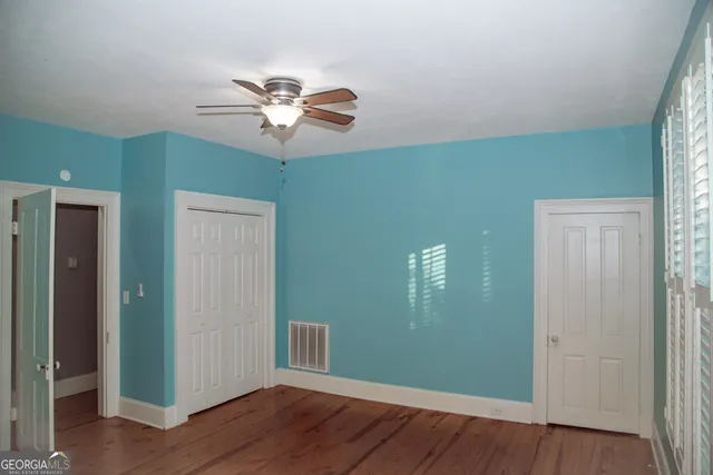 an empty room with wooden floor chandelier fan and windows