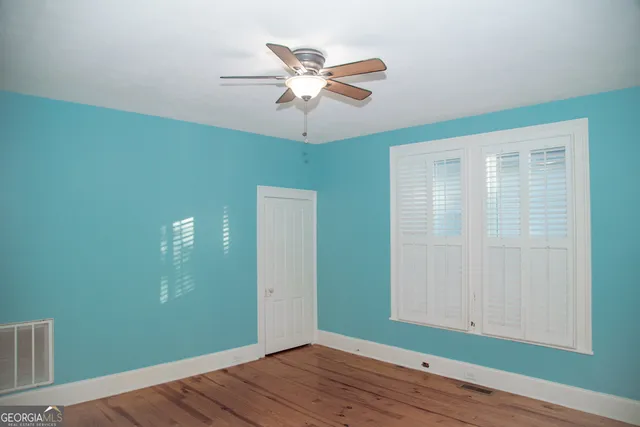an empty room with wooden floor chandelier fan and windows