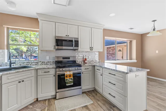 a kitchen with stainless steel appliances granite countertop white cabinets a sink a stove a microwave and wooden floors