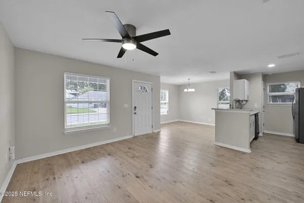 a view of a kitchen and an empty room with wooden floor and a window