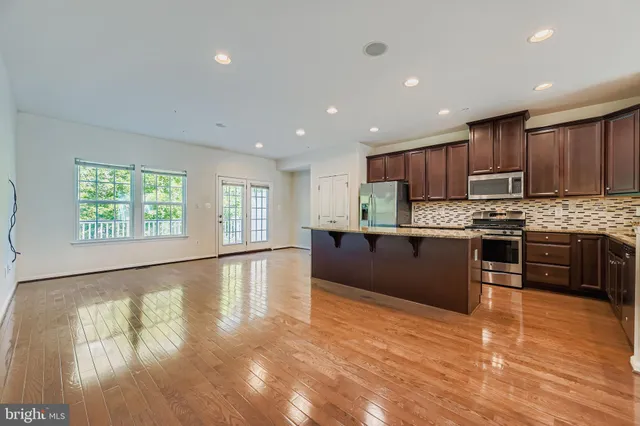a large kitchen with stainless steel appliances granite countertop a large counter top a stove a sink dishwasher and a refrigerator with wooden floor