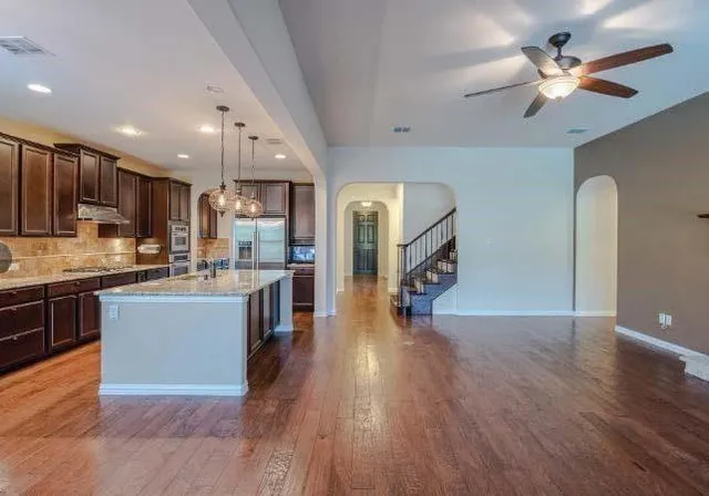 a kitchen with stainless steel appliances kitchen island granite countertop a stove a refrigerator a sink a microwave oven with wooden floor and cabinets