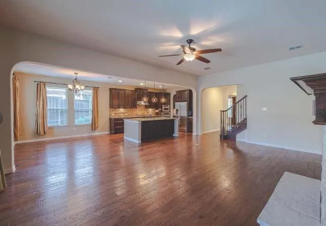 a view of an empty room with wooden floor and a kitchen