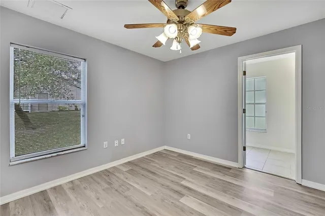 an empty room with wooden floor fan and windows
