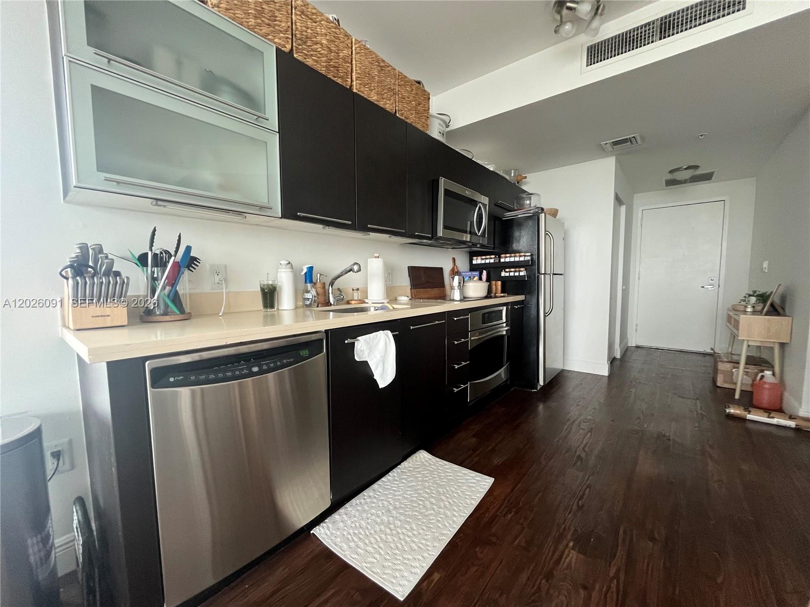 a kitchen with stainless steel appliances a sink dishwasher a refrigerator a stove and wooden cabinets with wooden floor
