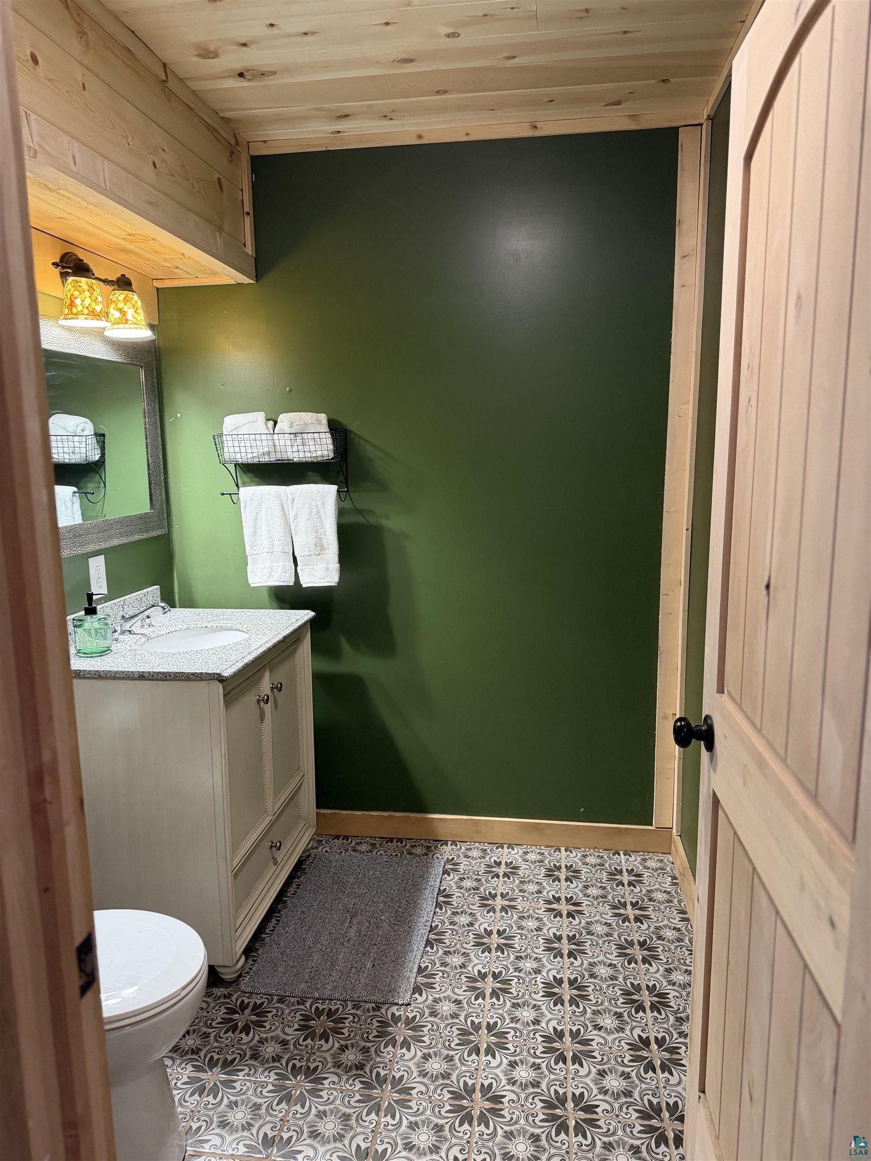 5274 Marble Lake Road Two Harbors, MN 55616 - Photo 38 of 79 Bathroom featuring a vanity with an integrated sink and light-colored countertop, decorative floor tiling, and a wooden plank ceiling