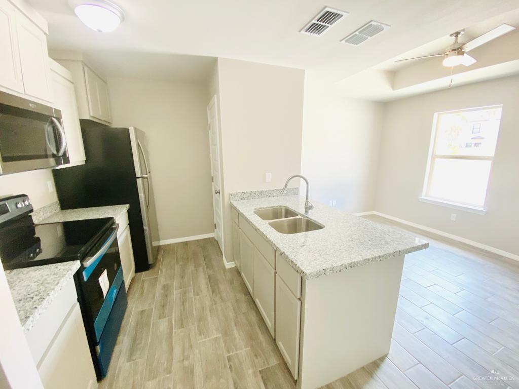 1105 West Kennedy Street, Unit 17 Pharr, TX 78577 - Photo 3 of 11 Kitchen featuring stainless steel appliances, a peninsula, light wood finished floors, light stone countertops, and a ceiling fan
