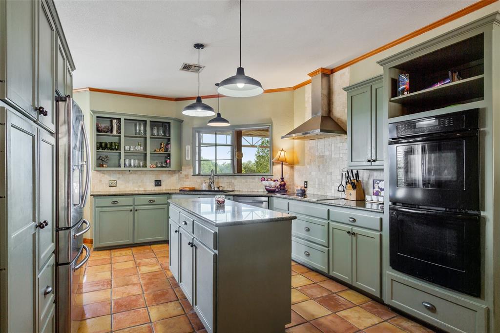 564 Sam Bass Road McGregor, TX 76657 - Photo 10 of 37 Kitchen featuring sage green cabinetry, a central island with a solid surface countertop, built-in stainless steel appliances, pendant lighting, and terracotta-style floor tiling