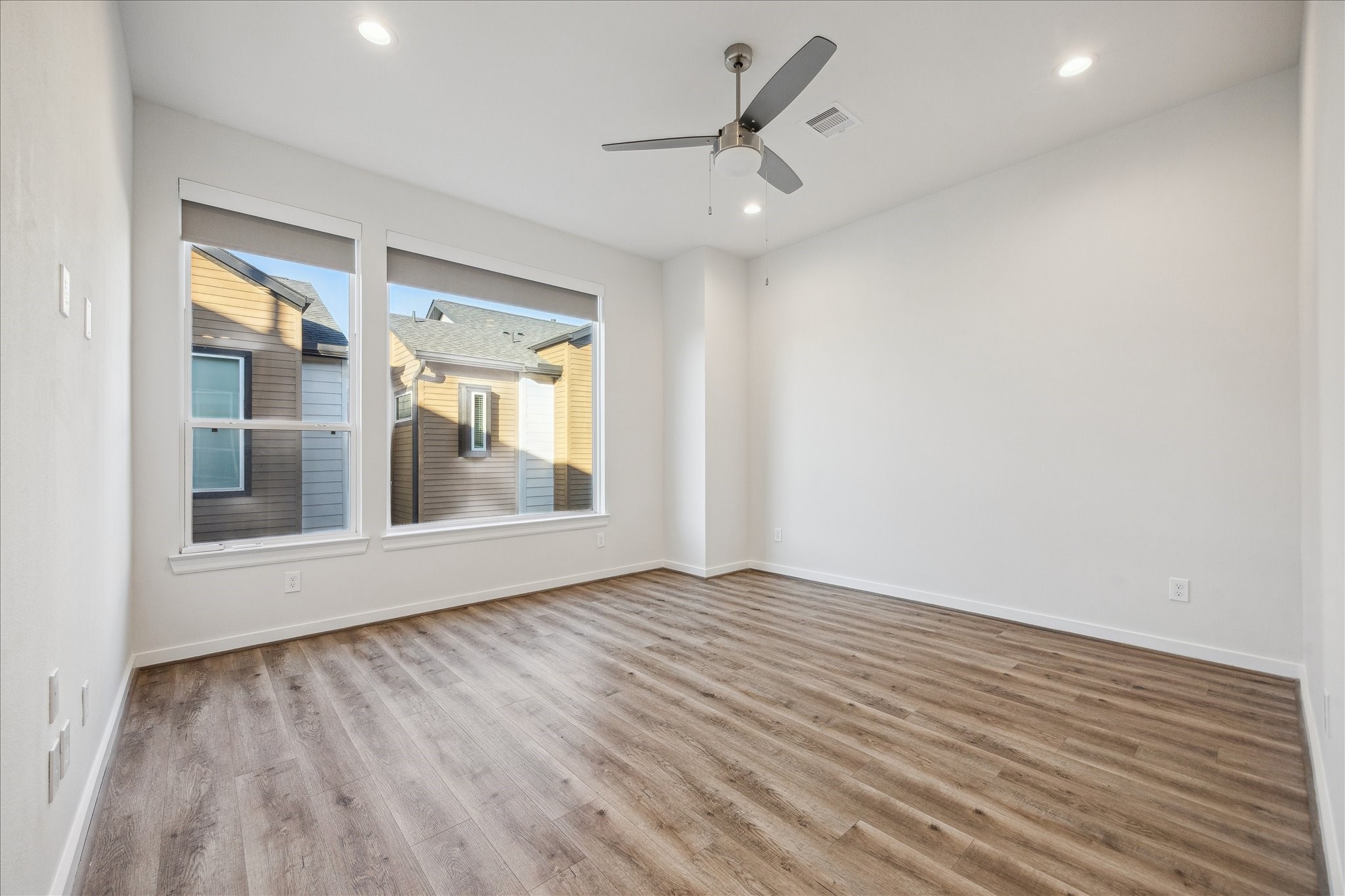 1603 Patterson Street, Unit E Houston, TX 77007 - Photo 27 of 32 This photo showcases a bright, spacious room with wood-style flooring, neutral walls, and recessed lighting. Large windows provide natural light, and a ceiling fan adds comfort. Ideal for a bedroom or office space.