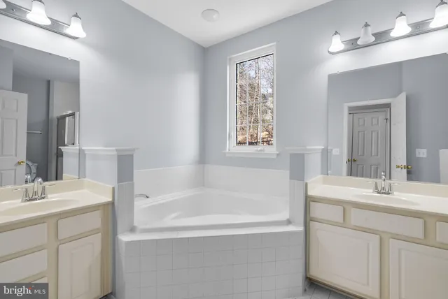 a bathroom with a bathtub a sink a vanity a window and mirror