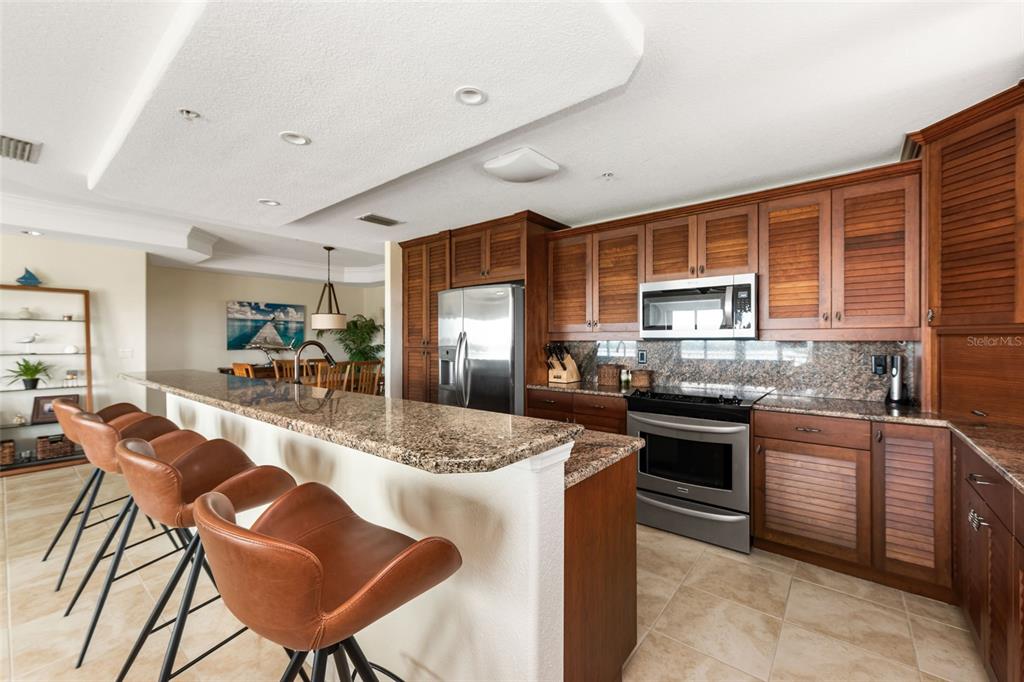 1420 Beach Road, Unit 204 Englewood, FL 34223 - Photo 29 of 99 a kitchen with stainless steel appliances granite countertop a stove top oven a sink dishwasher a dining table and chairs with wooden cabinets