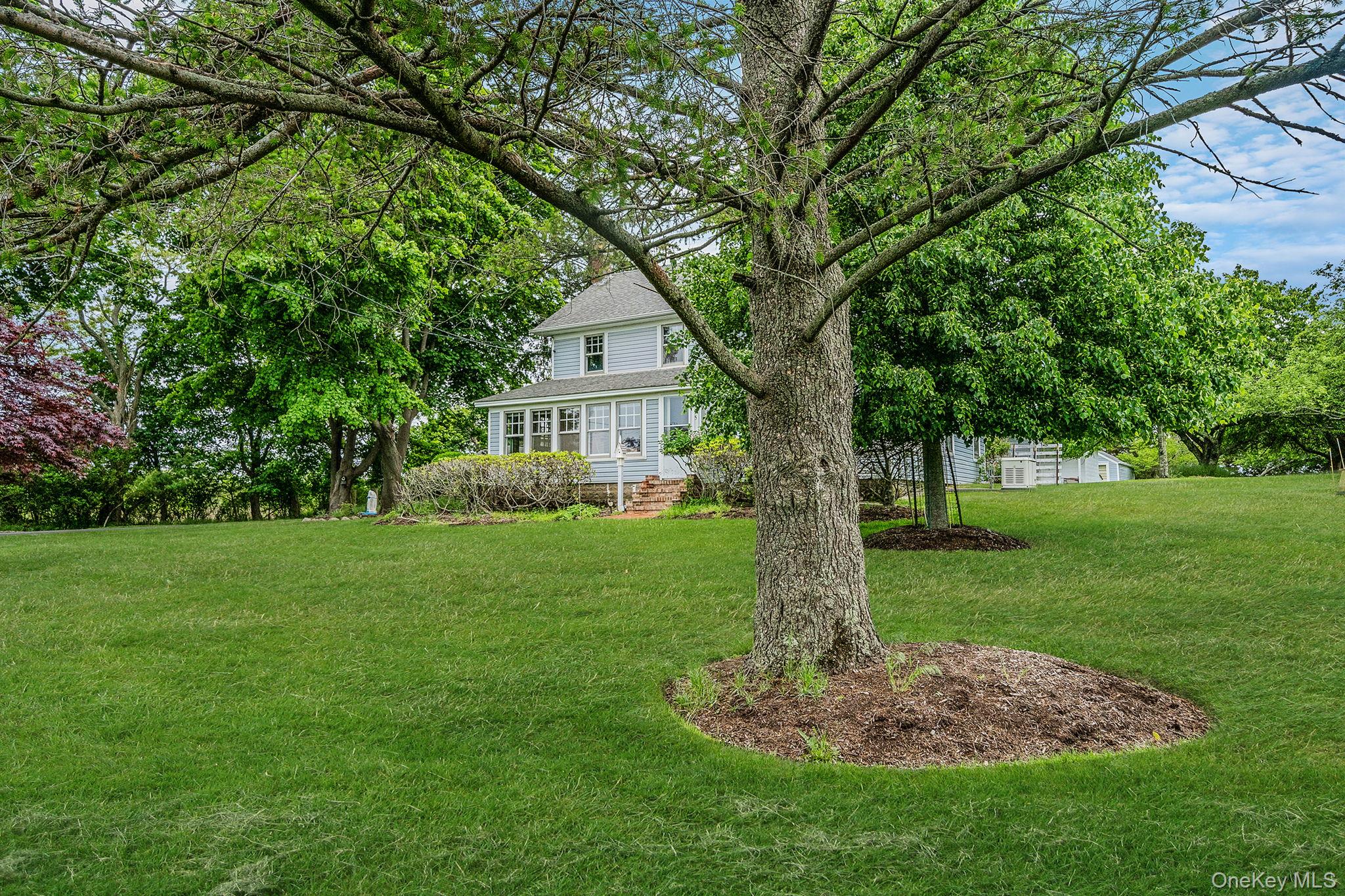1055 Oregon Road Mattituck, NY 11952 - Photo 29 of 33 Expansive green lawn with mature trees and a exterior residence featuring a covered porch. Many specimen trees.