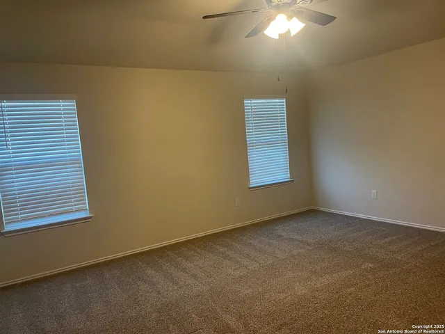 an empty room with chandelier fan and windows