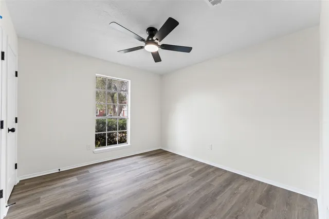 an empty room with wooden floor fan and windows